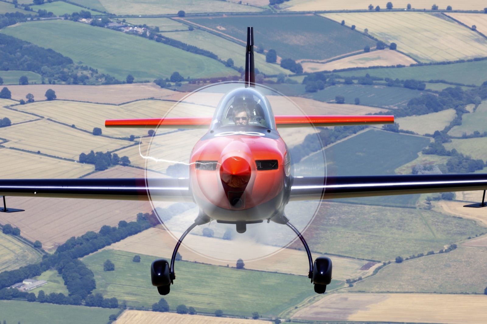 The Extra 300 head-on over the patchwork fields
