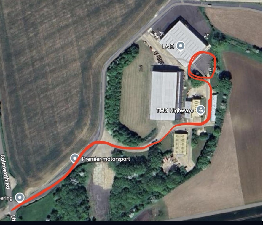 Aerial view of Little Staughton Airfield with the driving route marked in red from the airfield entrance, past Premier Motorsport and TMO Highways, to the car park behind the IAE hangar